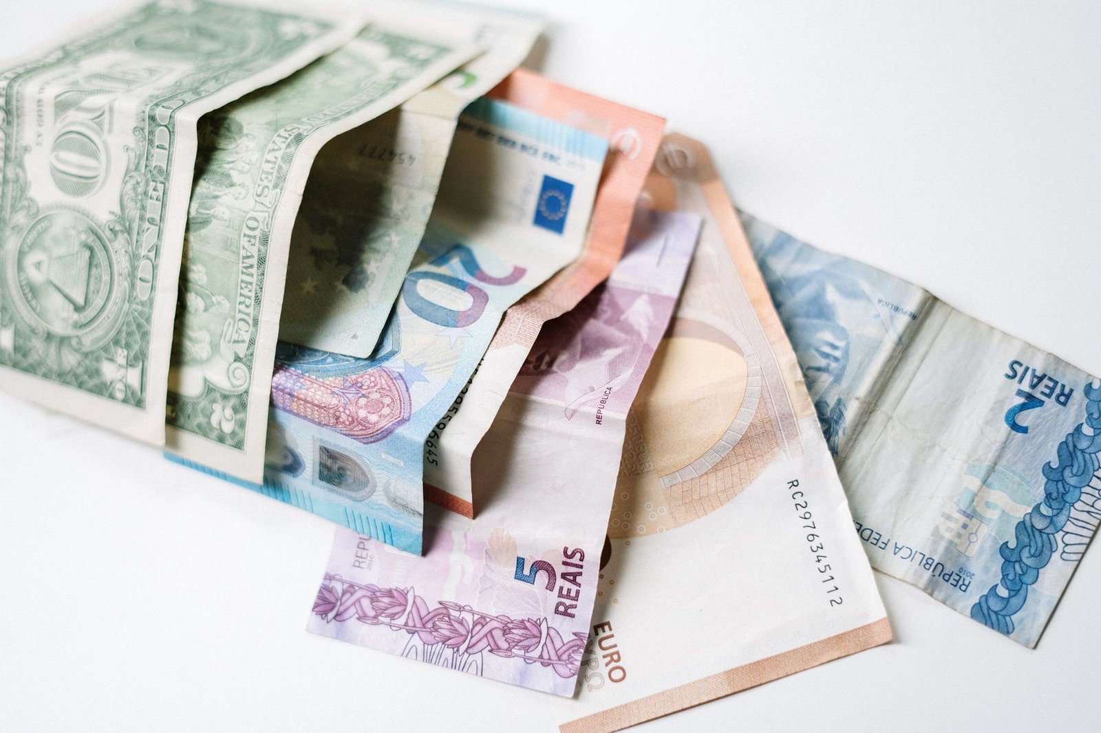 A collection of different international currency notes, including US Dollar, Euro, and Brazilian Real, on a white background.